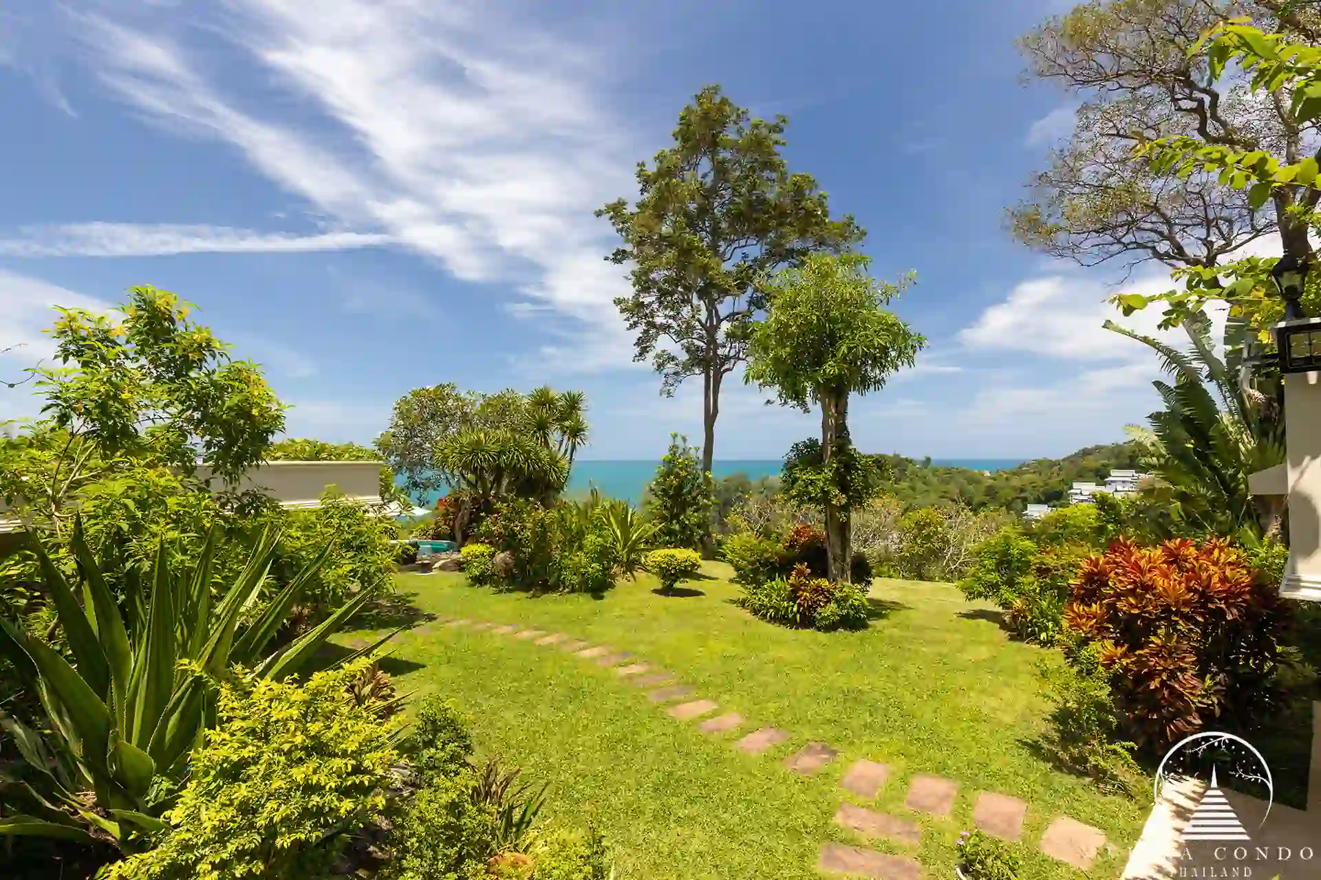 Garden area at Nakathani Villa Estate Kamala Beach with a sea view in the distance.